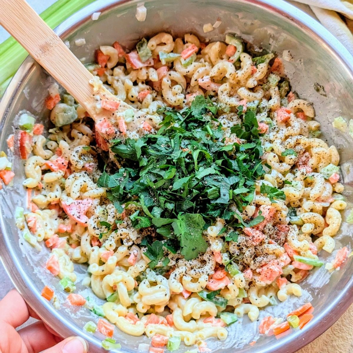 a bowl of vegetable macaroni salad with creamy dressing topped with fresh parsley and herbs to taste