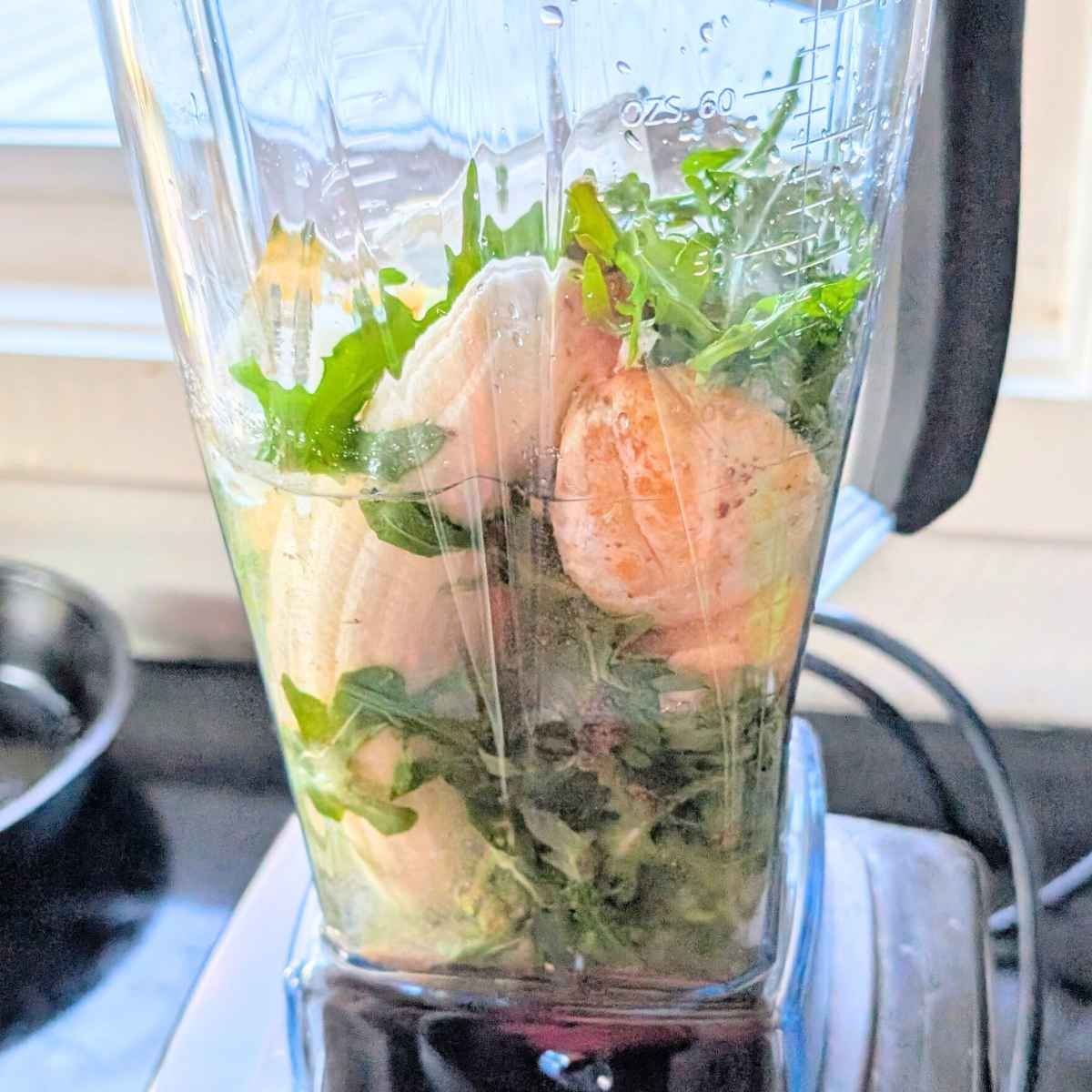 a blender filled with arugula, oranges, pineapple, water, and fruit.