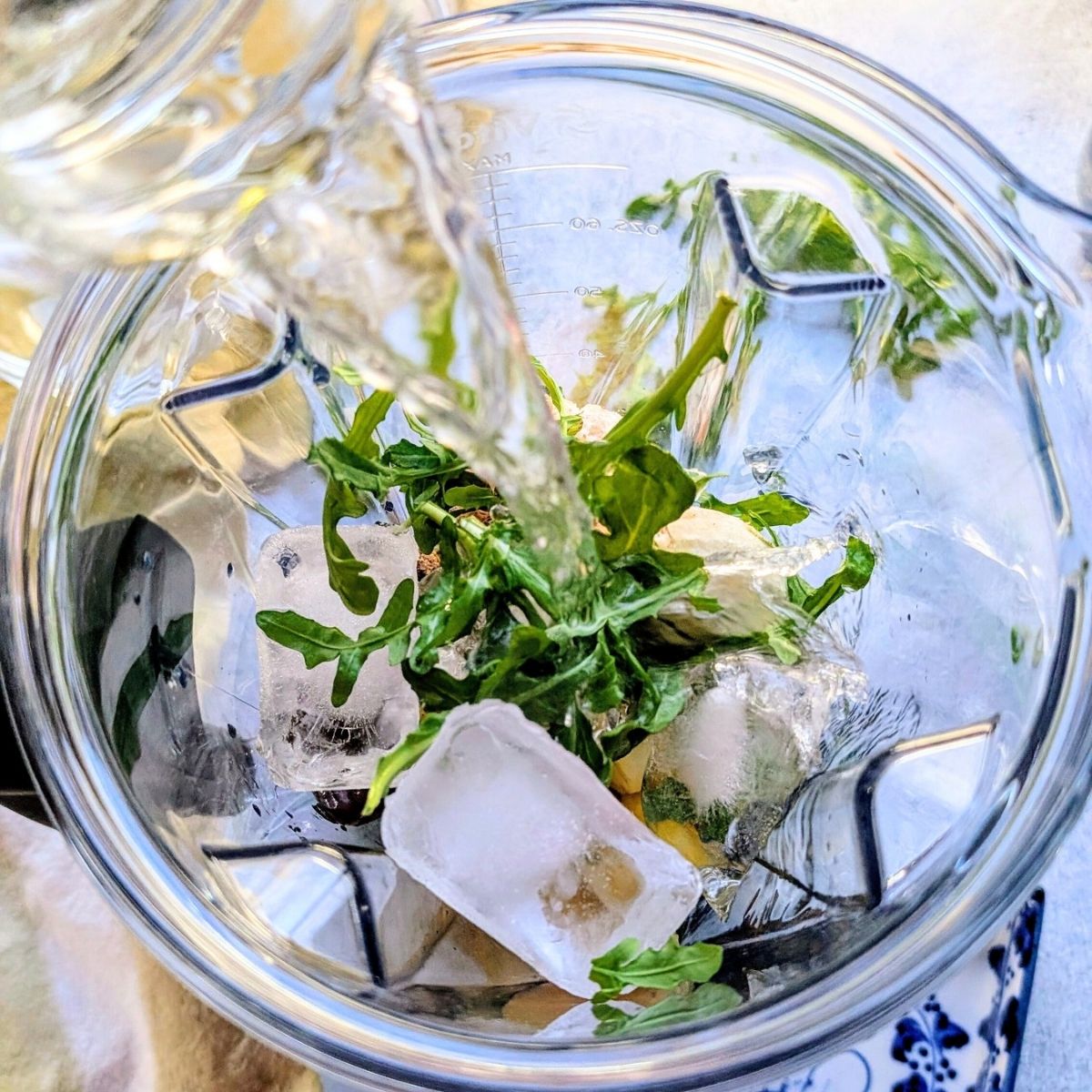 water being poured into a blender with ice and arugula smoothie recipe