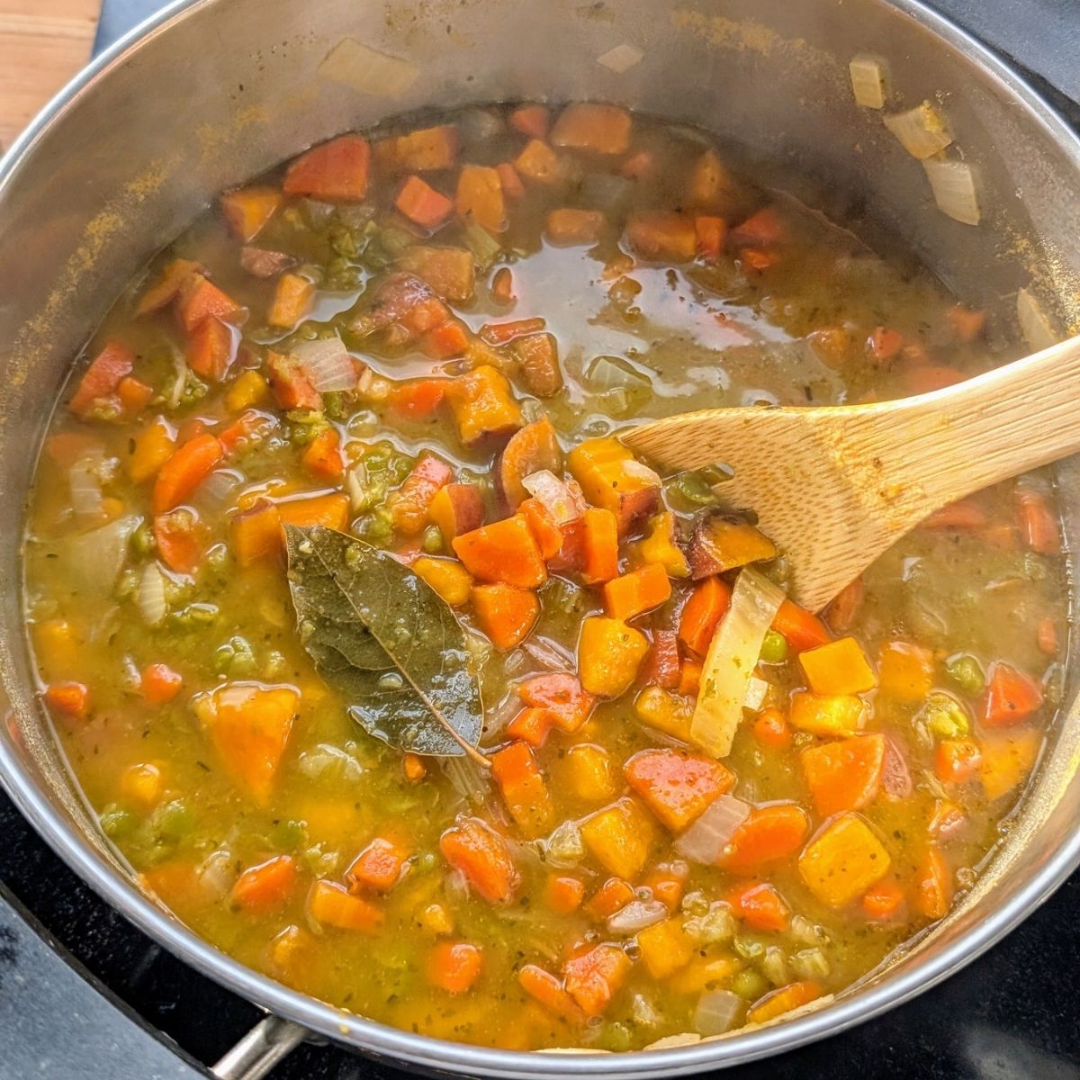 a pot of vegan and whole30 split pea soup with sweet potatoes and bay leaves and vegetables.