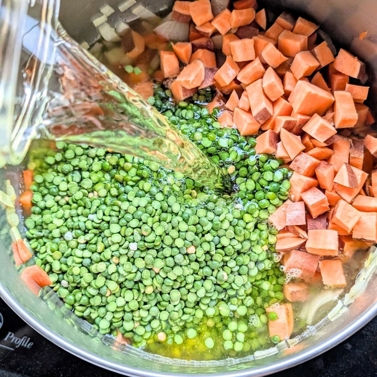 vegetable stock being added to a vegan split pea soup with sweet potatoes and onions