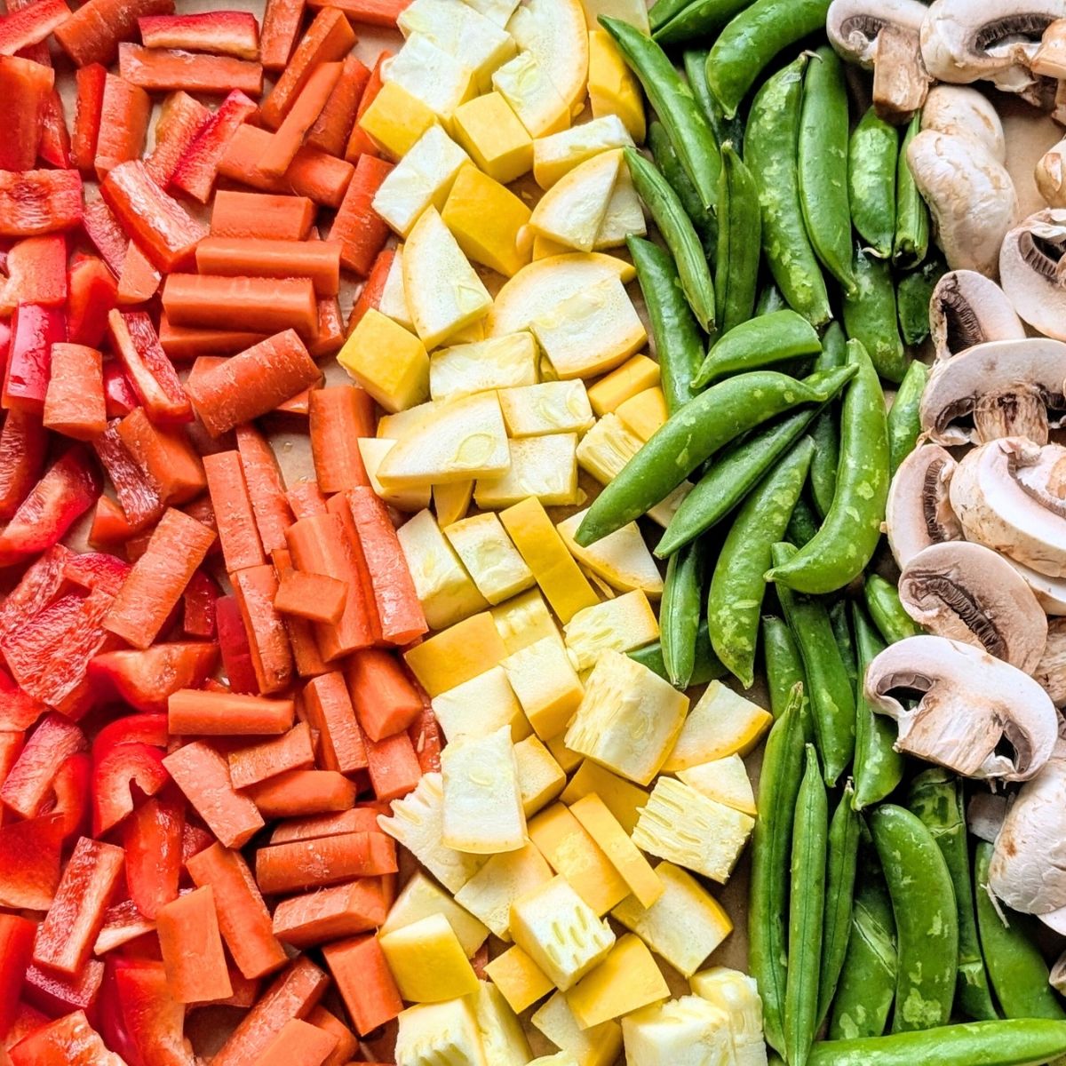 a pan full of red bell peppers, orange carrots, yellow squash, green snap peas, mushrooms, and red onions