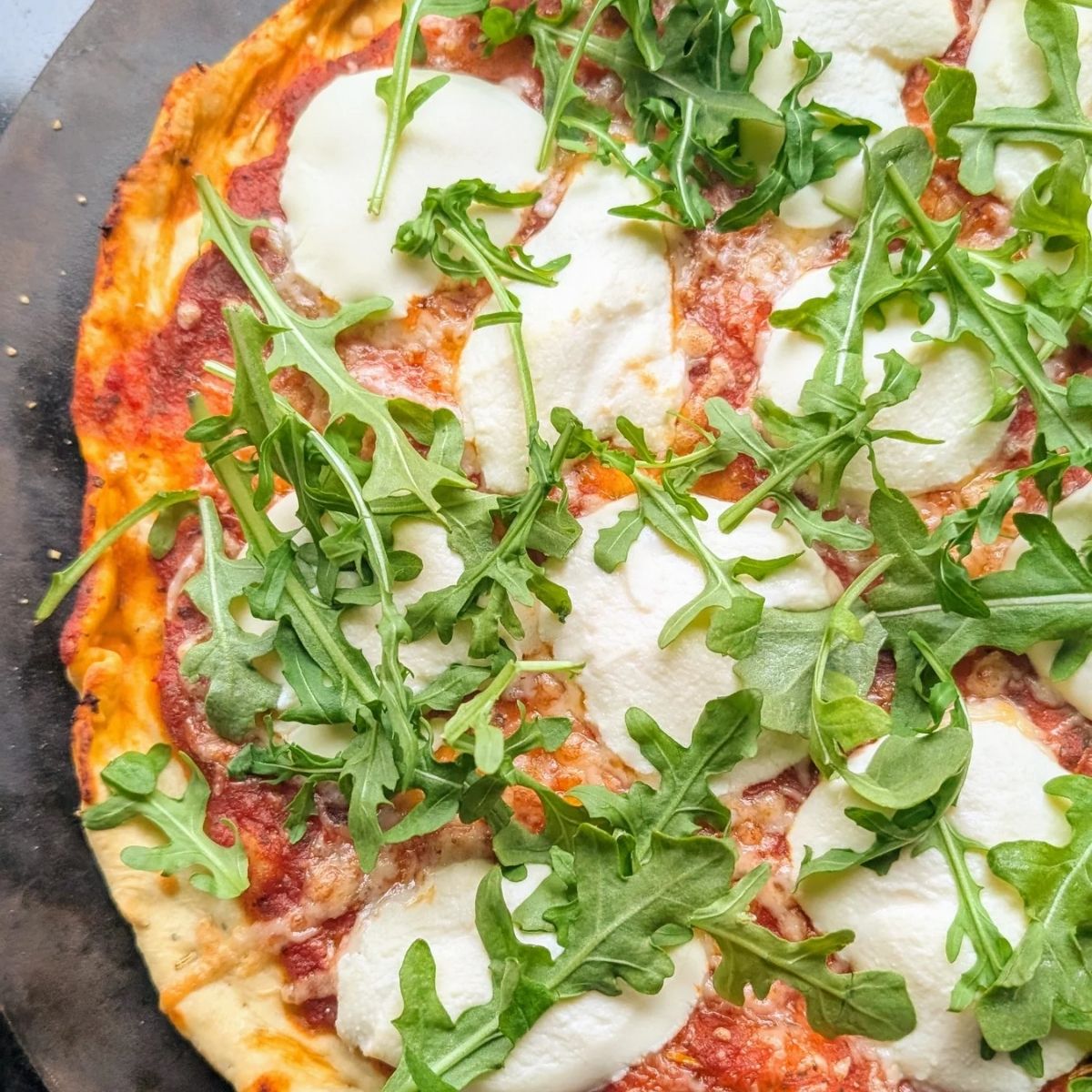 fresh arugula on top of ricotta hot honey pizza with chili flakes