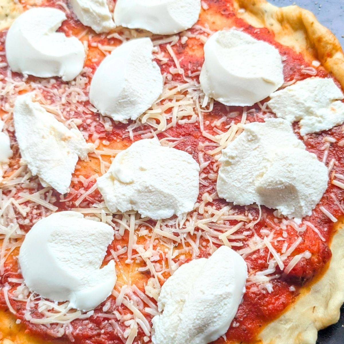 ricotta cheese on tomato pizza with parmesan cheese and a half baked crust