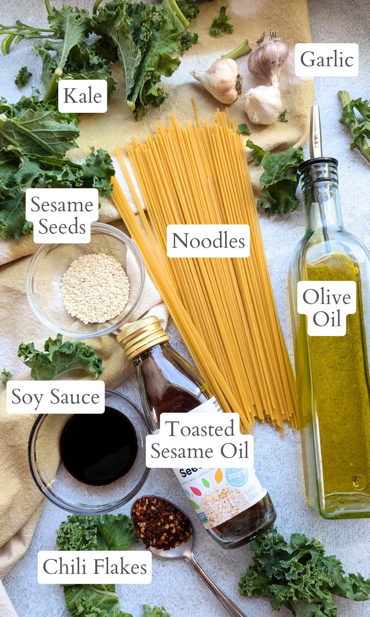 ingredients for kale noodle recipe like pasta, olive oil, sesame seeds, soy sauce, and fresh kale