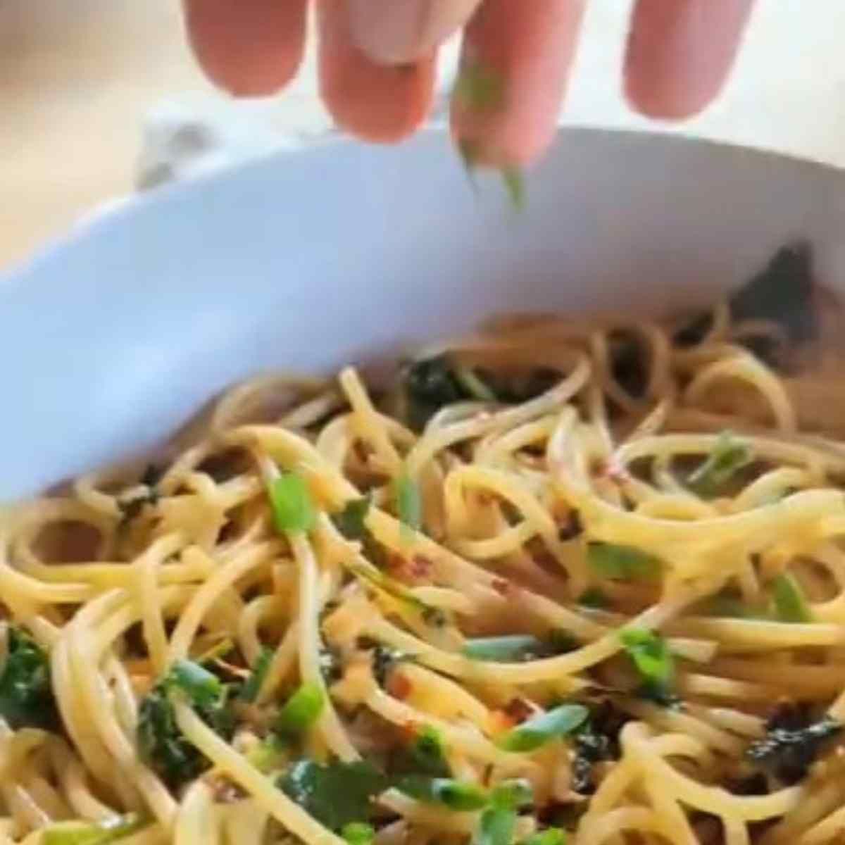 a hand sprinkling green onions over kale noodles in a bowl for vegan dinner