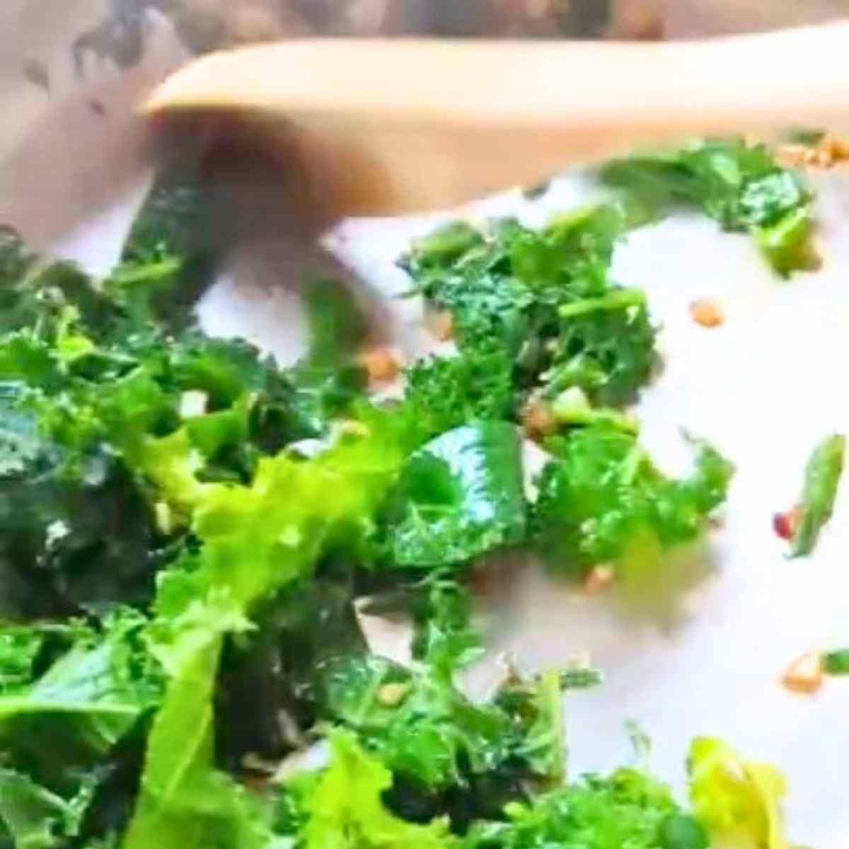 kale sauteeing in a pan with garlic chili flakes and sesame oil