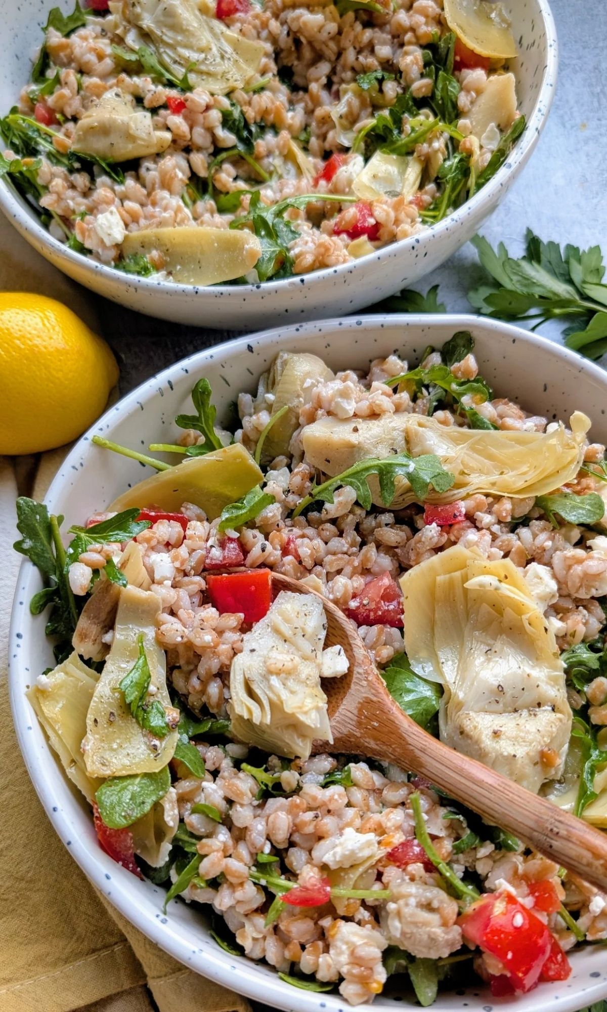 a spoon serving a grain and artichoke salad with farro and vegetable salad that can be served warm or cold.