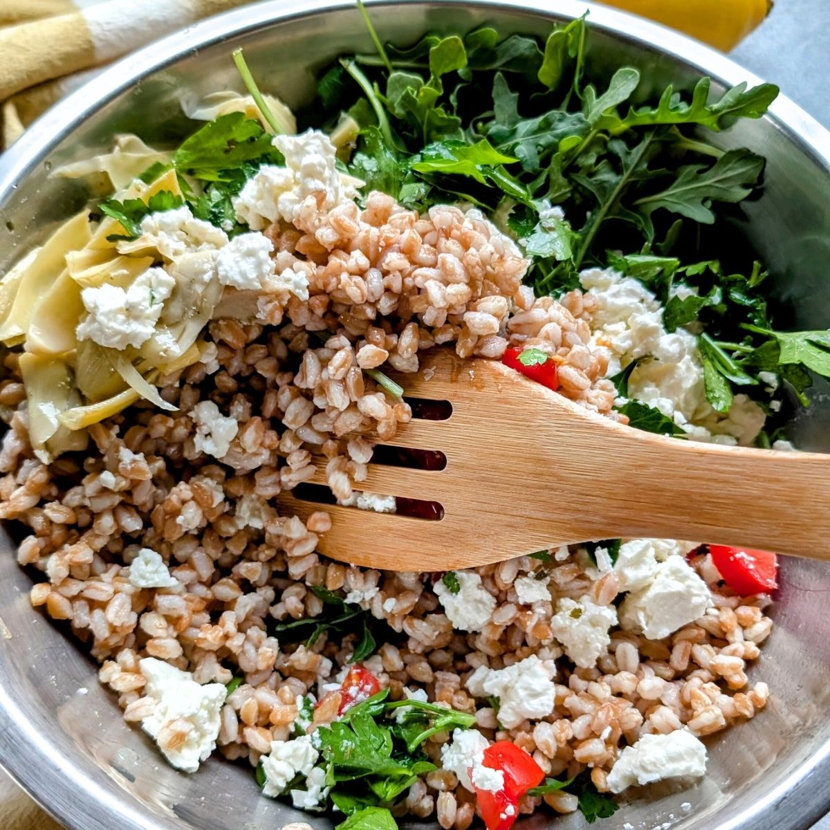 a spoon stirring farro and artichoke salad with arugula the best farro salad with feta cheese.