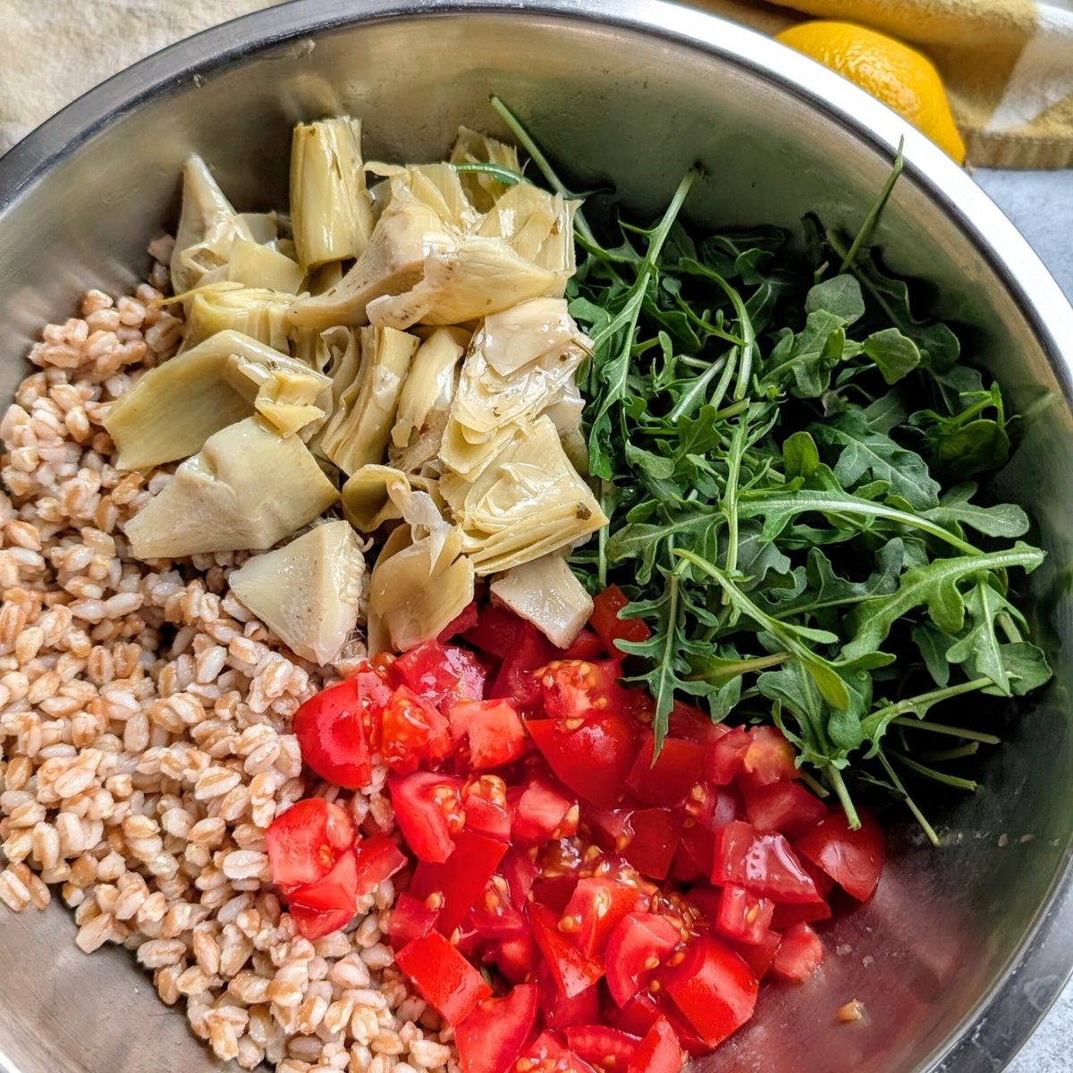 a large mixing bowl of cooked farro, arugula, fresh chopped tomatoes, and artichoke hearts.