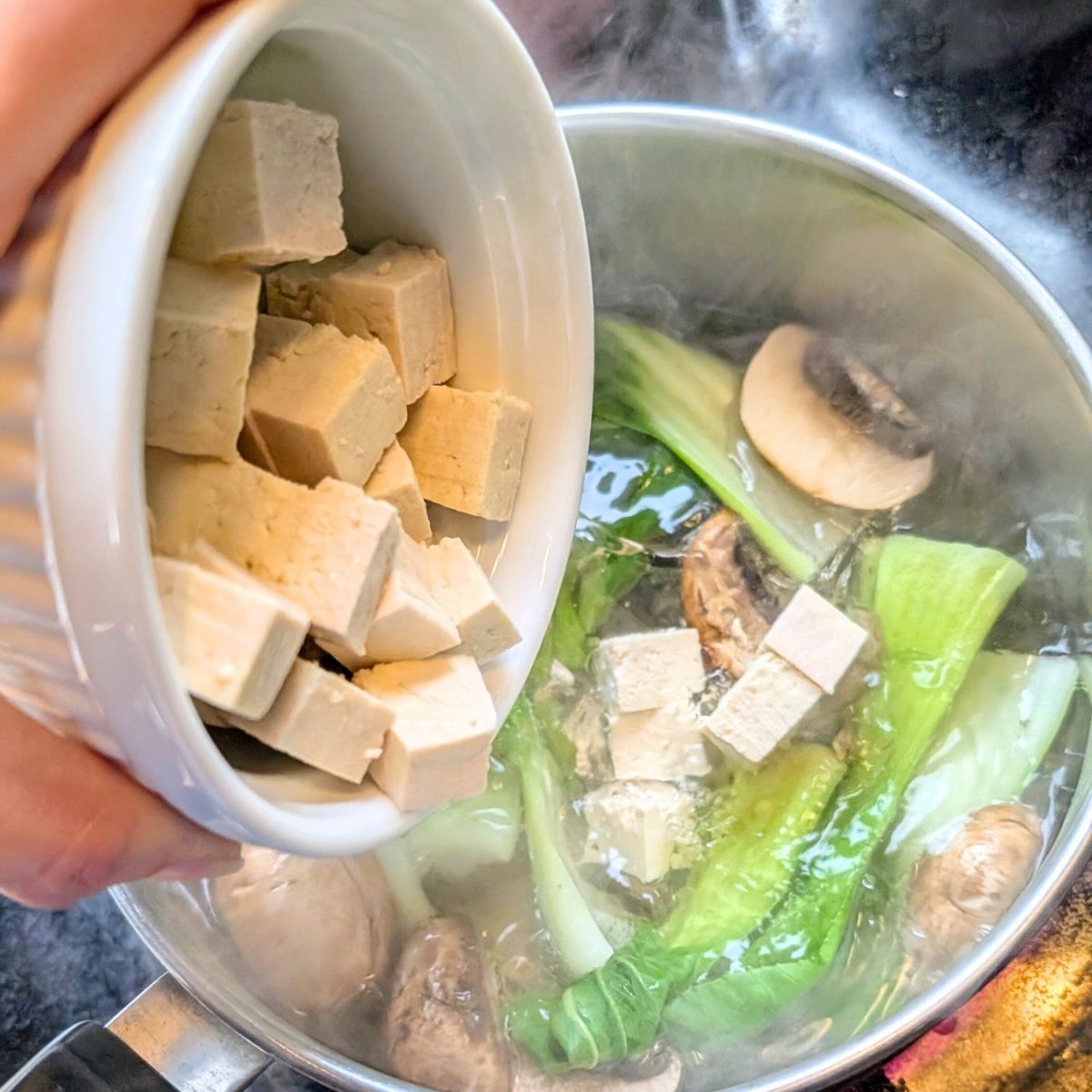 tofu being added to miso mushroom soup with fresh greens and mushrooms, shiitake or cremini