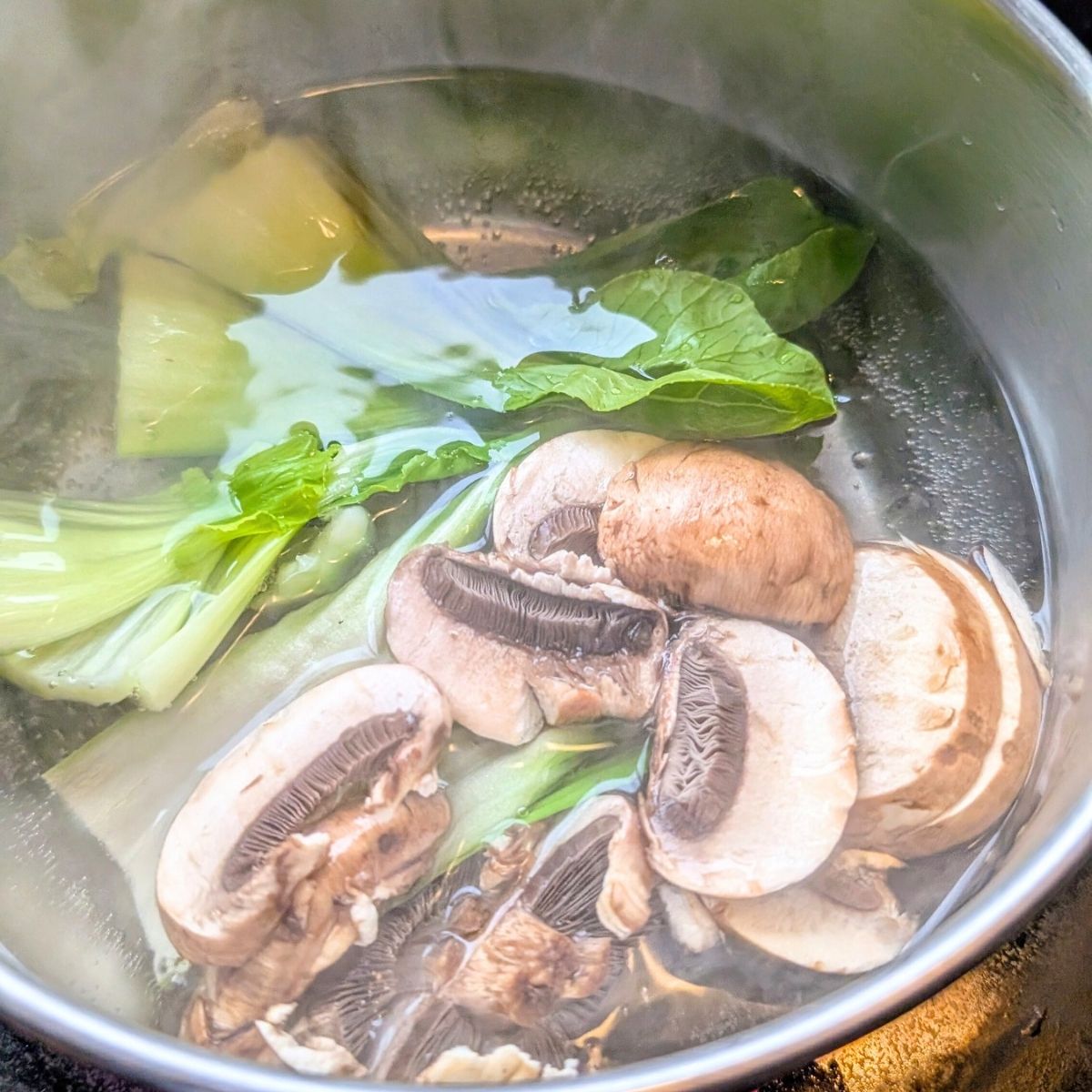 a big pot of miso soup with mushrooms and bok choy boiling on the stovetop.