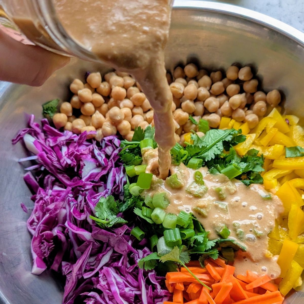 peanut dressing poured over crunchy chickpea salad with cabbage and carrots in a large mixing bowl.