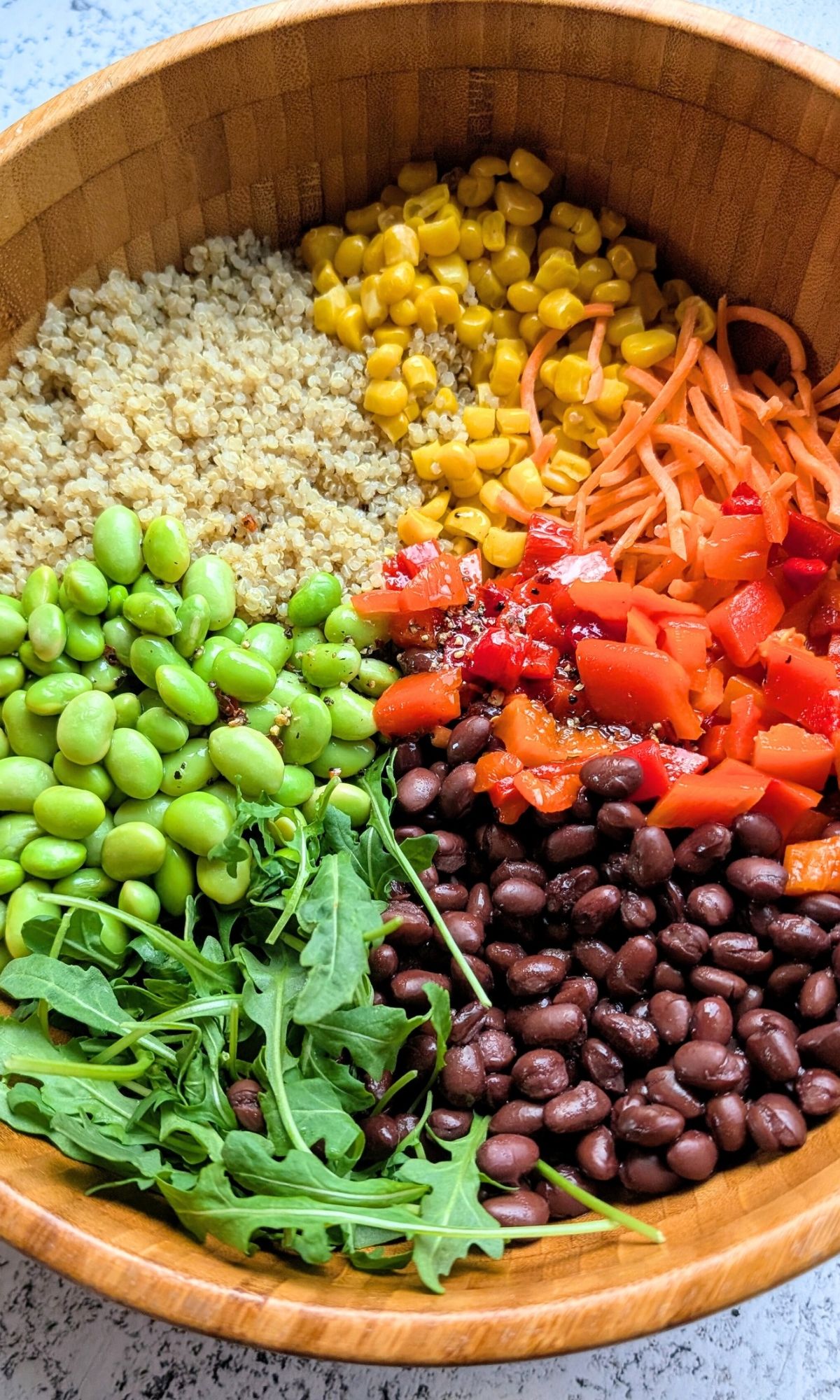 a large bowl of quinoa, black beans, corn, carrots, arugula, and roasted red bell peppers.