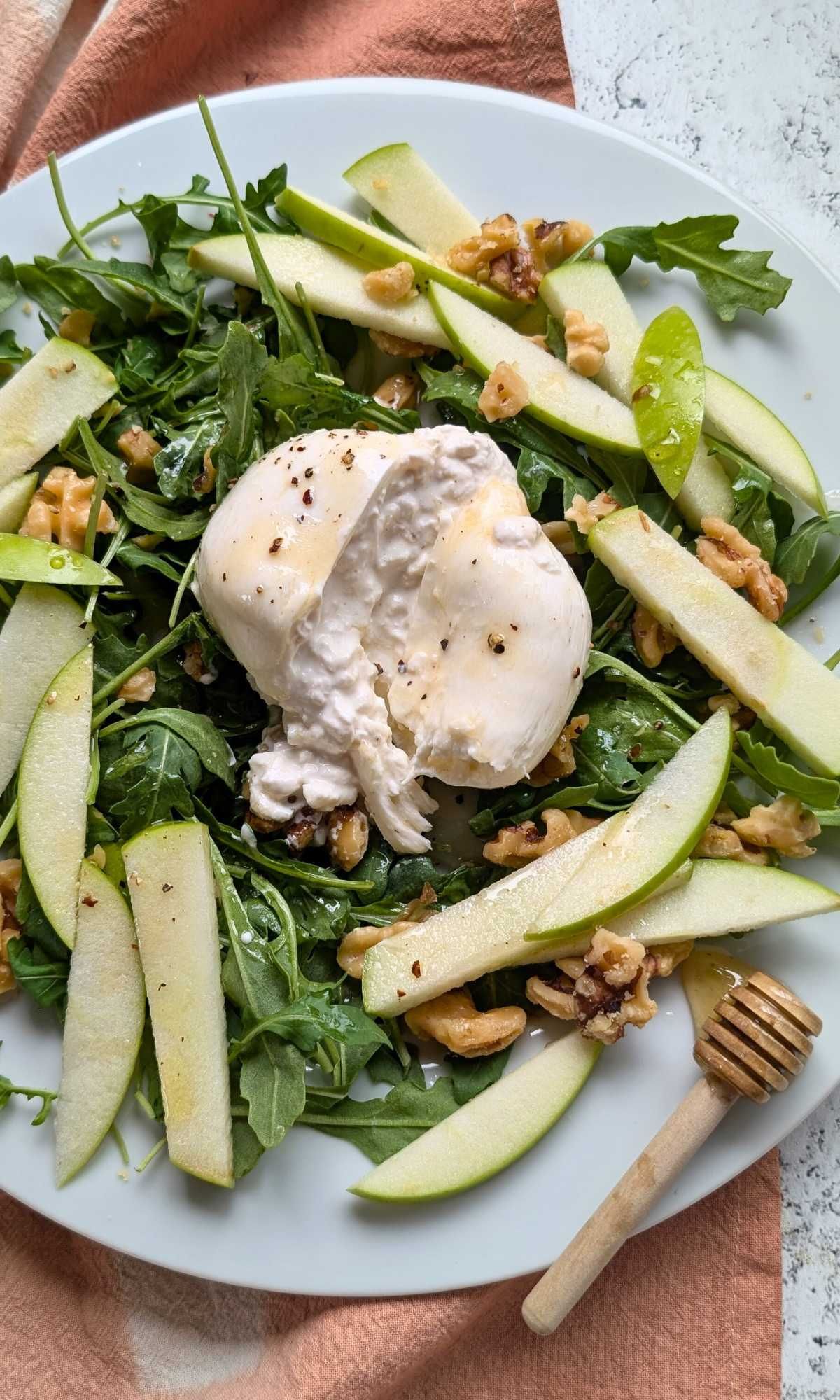 creamy burrata cheese on a plate with honey and arugula with sliced apples for a summer light elegant salad.