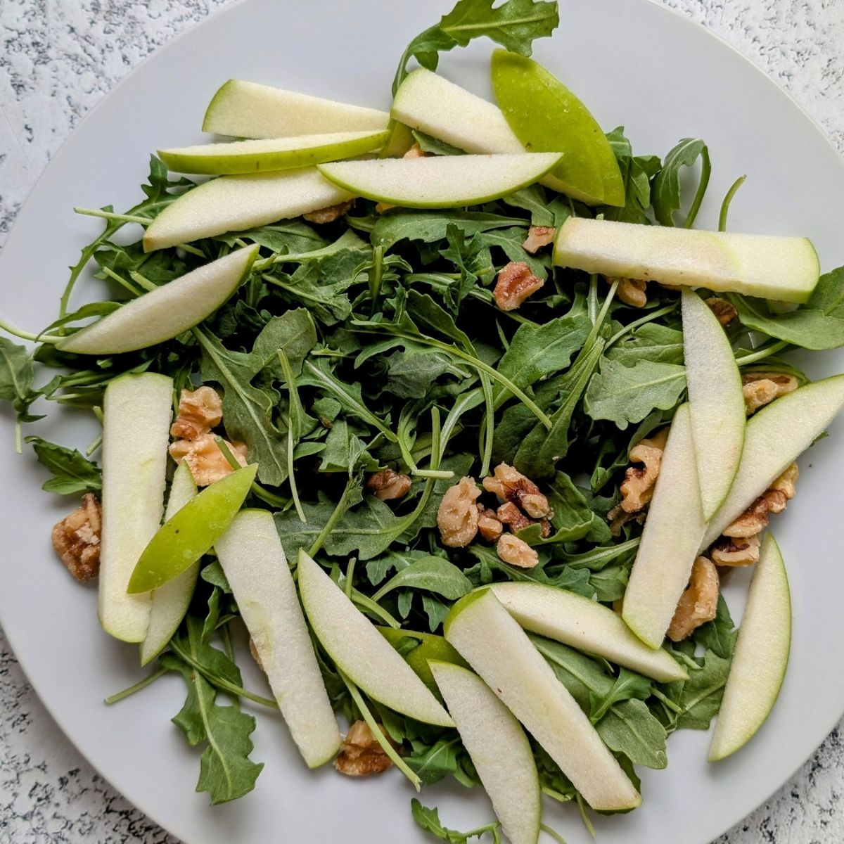 a plate with baby arugula, thinly sliced granny smith apple, and walnuts in a wreath formation.