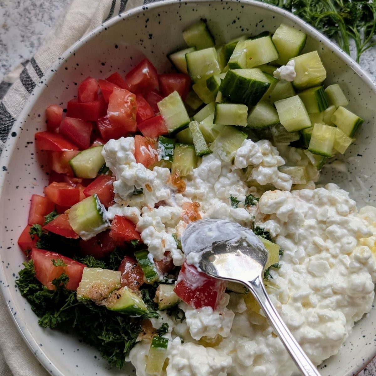 a spoon mixing cottage cheese and vegetable salad in a bowl for a tasty high protein vegetarian breakfast idea.