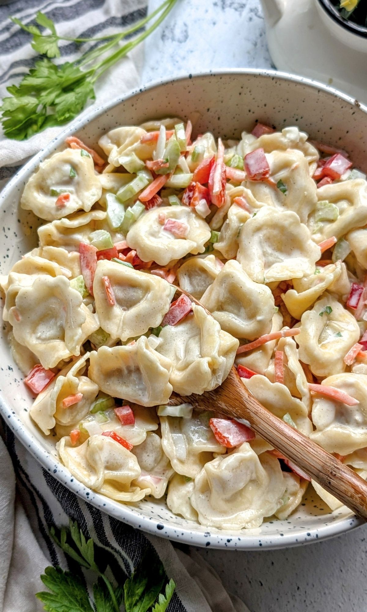 a bowl of creamy tortellini salad with vegetables and mayo dressing.