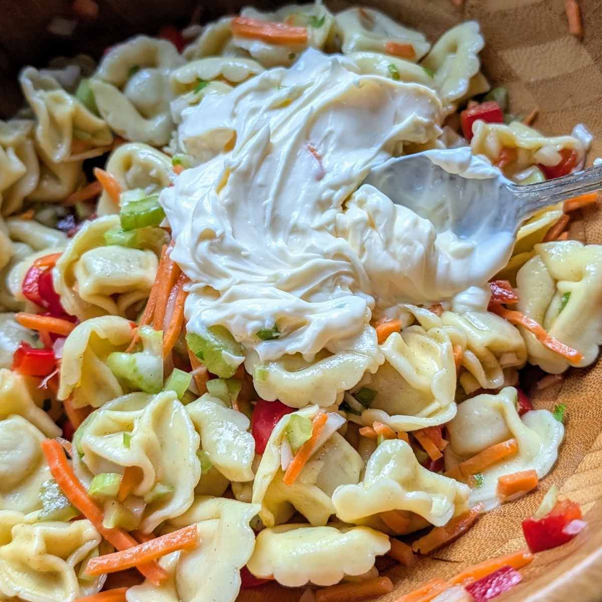 mayonnaise stirred into tortellini salad with vegetables.