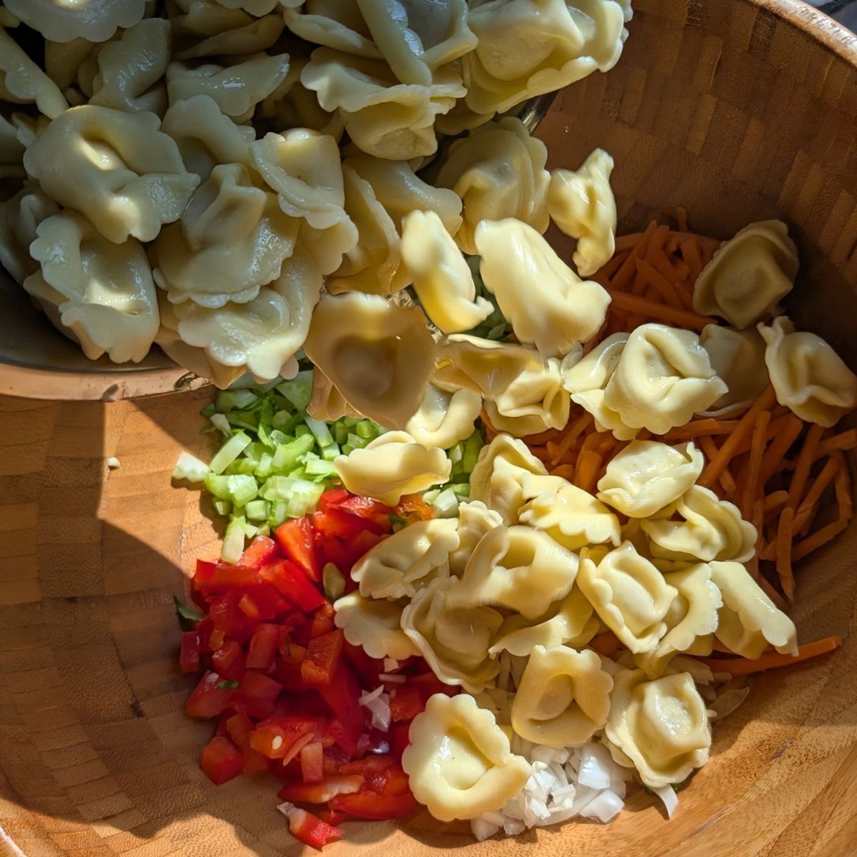 cooked tortellini in a bowl with fresh vegetables to make pasta salad.