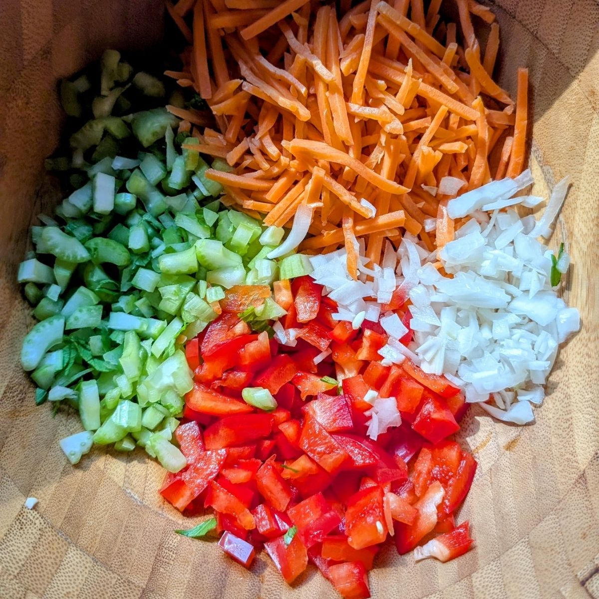 a bowl of chopped carrots, celery, red bell pepper, and white onions in a bowl.