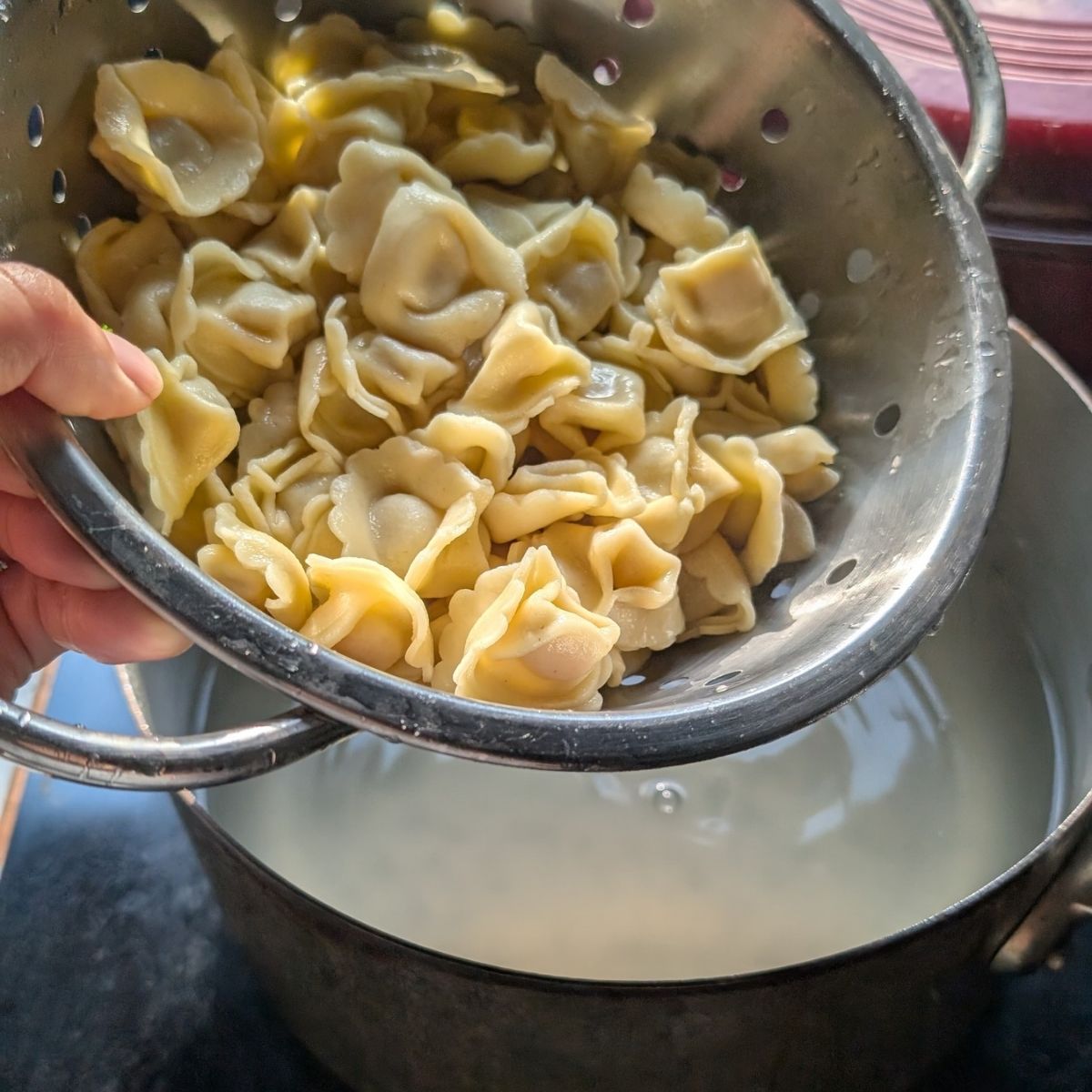cooked tortellini in a pot being drained and cooled for pasta salad.