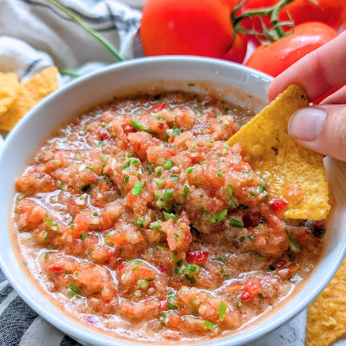 garlic scape pico de gallo salsa recipe with a hand dipping a tortilla chip into it
