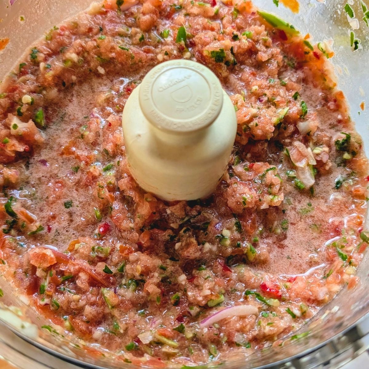 a food processor full of salsa with garlic scapes and tomatoes and herbs.