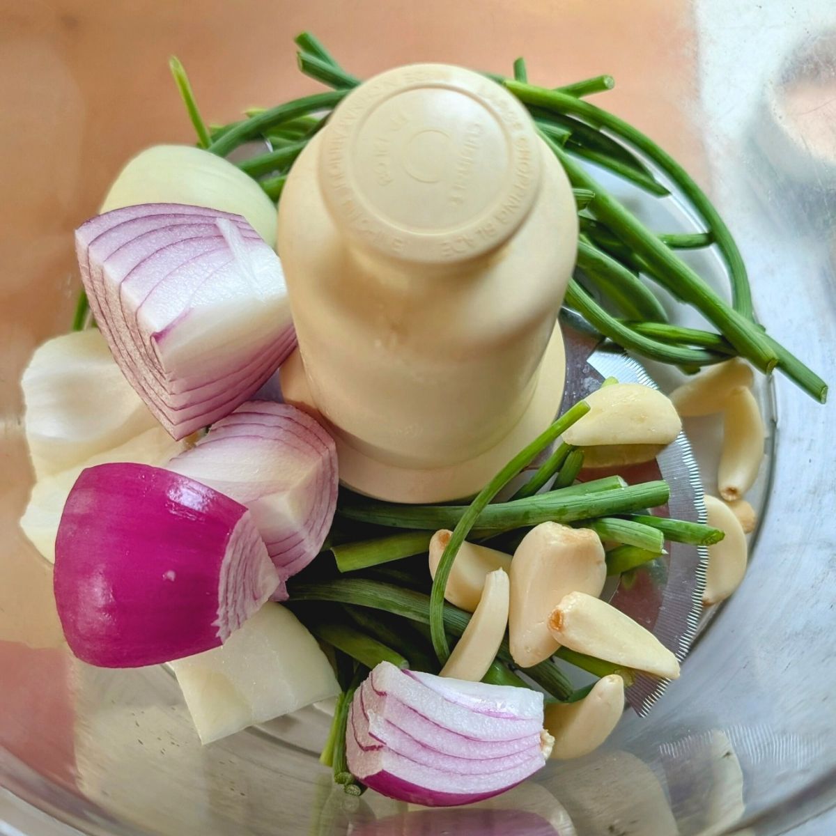 a food processor full of garlic scapes, fresh garlic cloves, and onions.
