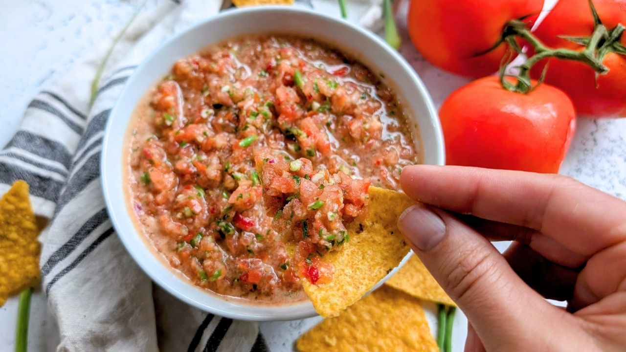 a tortilla chip being dipped in garlic scape salsa with tomatoes and peppers.