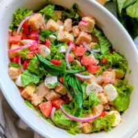 focaccia panzanella salad with tomatoes, greens, and pickled onions in a large dish