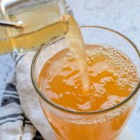 a glass of homemade ginger kombucha being poured into a cup from a kombucha bottle