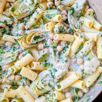a pan of creamy rigatoni noodles with chickpeas, spinach, and artichokes in a cream cheese sauce