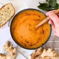red lentil ginger soup recipe bring stirred by a hand with coconut milk