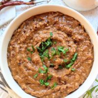 Refried pinto beans in a bowl with fresh cilantro and chili flakes on top