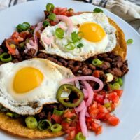 Huevos rancheros with pinto bean salsa and pickled red onions on a fried tortilla with a fried egg, sunny-side up.